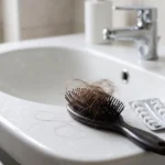Haaruitval door medicijnen: haarborstel met uitgevallen haar naast tabletten op de wastafel.